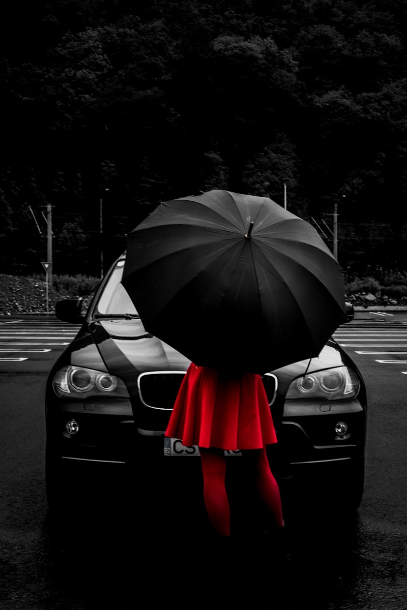 woman wearing red flare dress under black umbrella while standing in front of vehicle symbolizing umbrella insurance policy